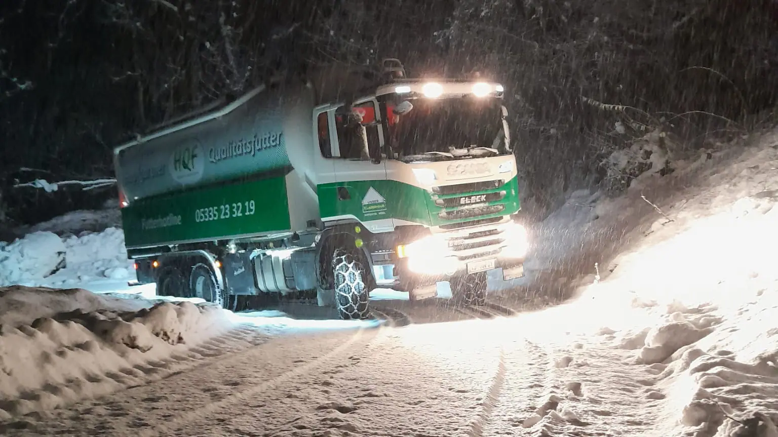 HQF-Silo-LKW mit Schneeketten bei Nacht auf einer verschneiten Bergstraße